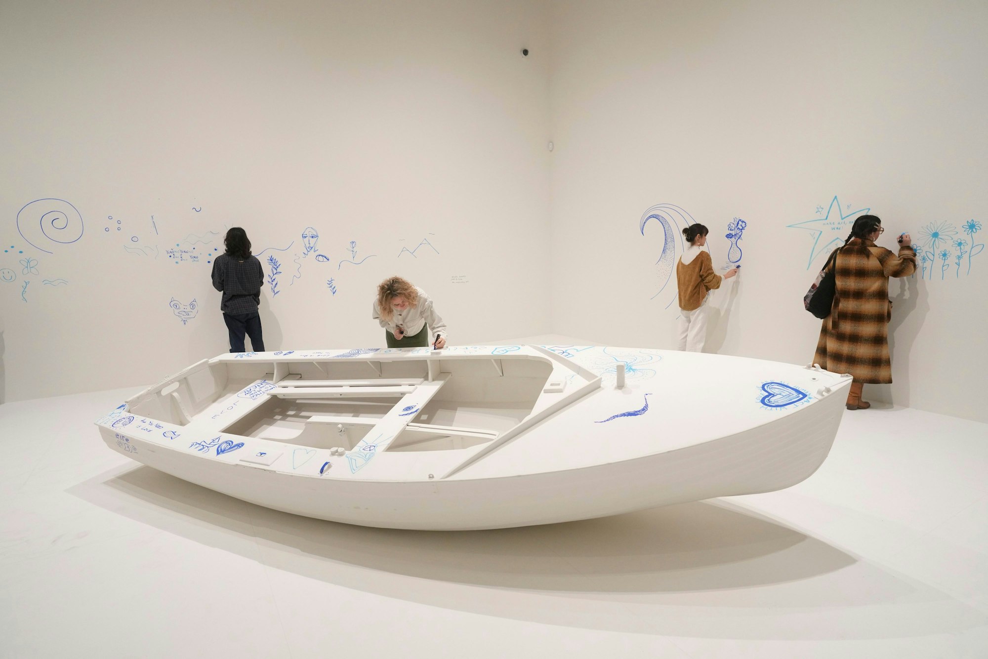 Members of staff draw on a work entitled Add Colour (Refugee Boat), Concept 1960, first realised 2016, exhibition realisation 2024, at the Yoko Ono : Music of the Mind exhibition at the Tate Modern, the works of art are copyright Yoko Ono, In London, Tuesday, Feb. 13, 2024. The exhibition which has many pieces that are interactive and the public and which participate in, runs from Feb.15, to Sept. 1. (AP Photo/Alastair Grant)