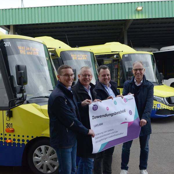 Norbert Reinkober, Marcel Frank, Anno Schichler-Koep und Sacha Reichelt stehen vor mehrern blau-gelben Bussen und halten einen Zuwendungsbescheid in der Hand.