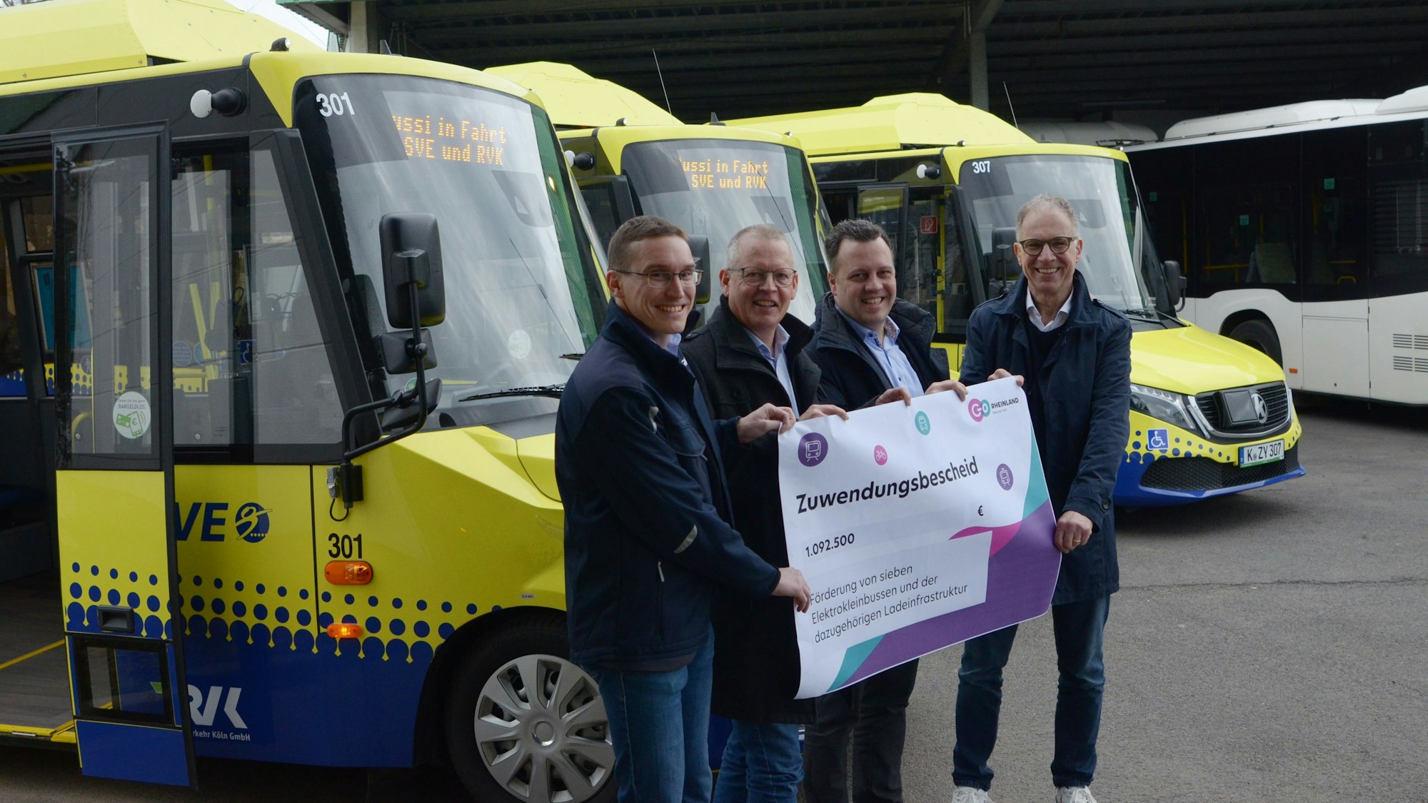 Norbert Reinkober, Marcel Frank, Anno Schichler-Koep und Sacha Reichelt stehen vor mehrern blau-gelben Bussen und halten einen Zuwendungsbescheid in der Hand.