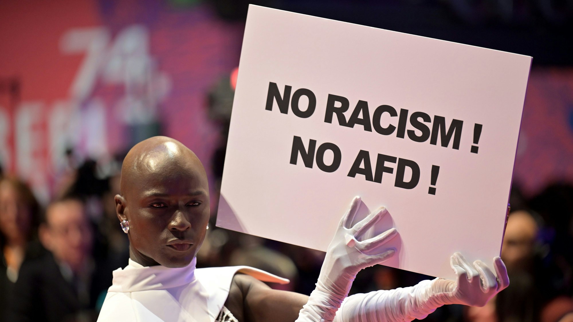 Papis Loveday steht am Eröffnungsabend der Berlinale mit einem Protestschild „No Racism ! No AFD !“ auf dem Roten Teppich. Es wird der Film „Small Things Like These“ gezeigt