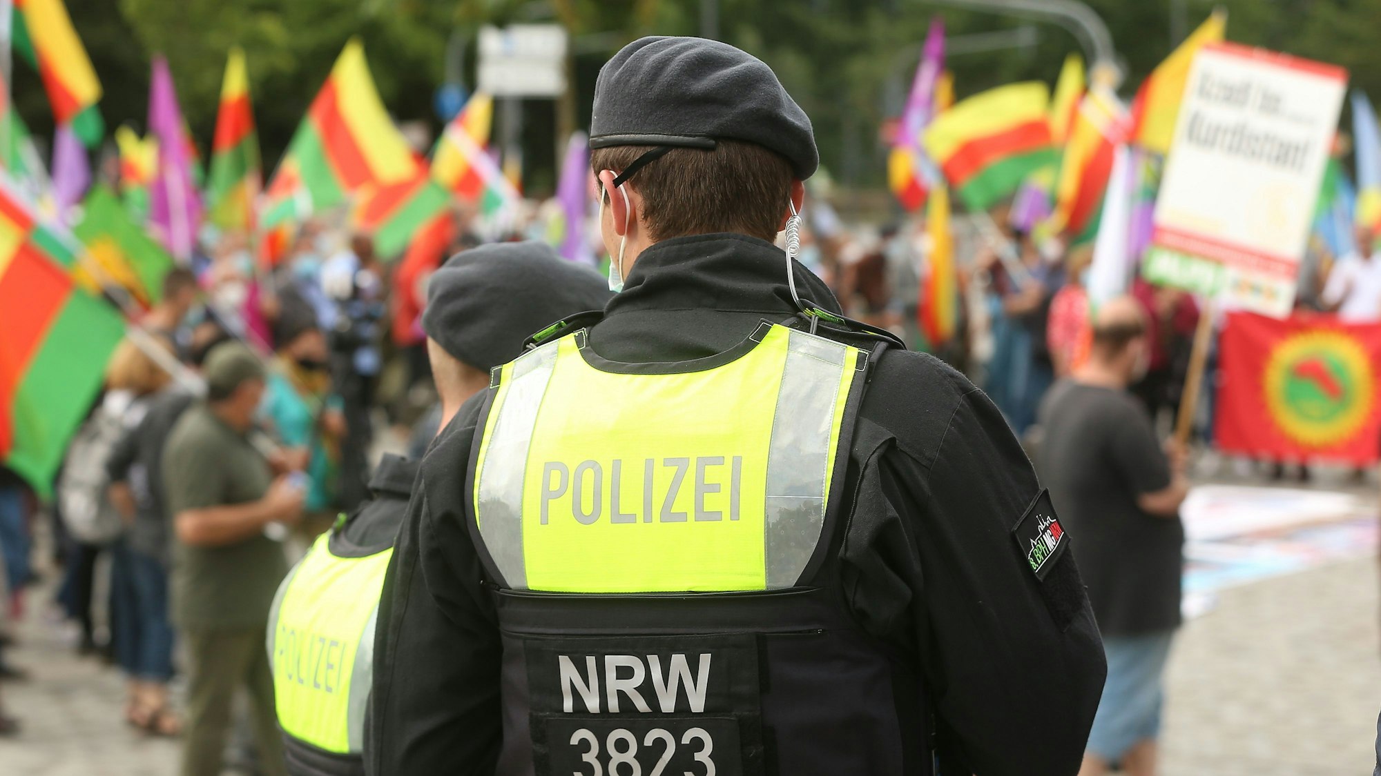 Im Sommer 2021 hatten Kurden auf dem Ottoplatz in Deutz demonstriert. Nun steht eine Großkundgebung auf dem Ottoplatz an. Zu sehen ist ein Polizist und Demonstrierende mit Fahnen.