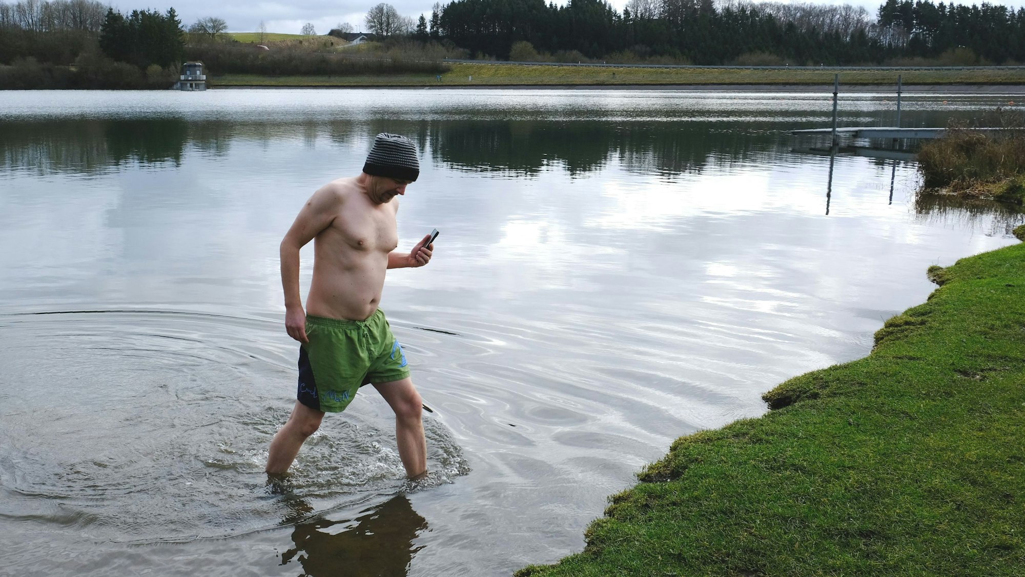 RRG-Redakteur Thorsten Wirtz mit Wollmütze und Badehose beim Verlassen des Freilinger Sees. In der Hand hält er ein Handy.