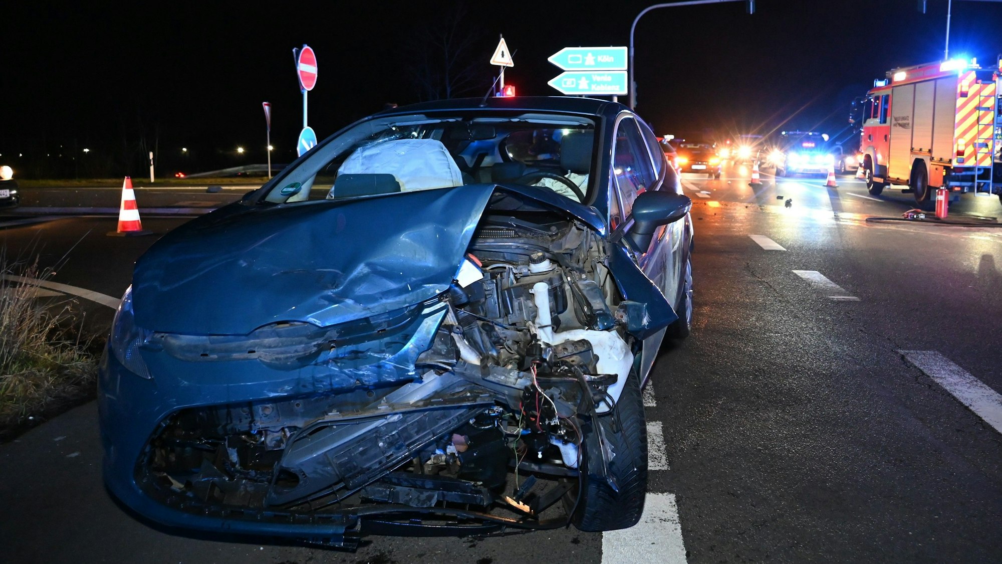 Ein blauer Pkw steht schwer beschädigt auf einer Straßenkreuzung in der Nacht. Die vordere linke Seite ist verbogen und kaputt.