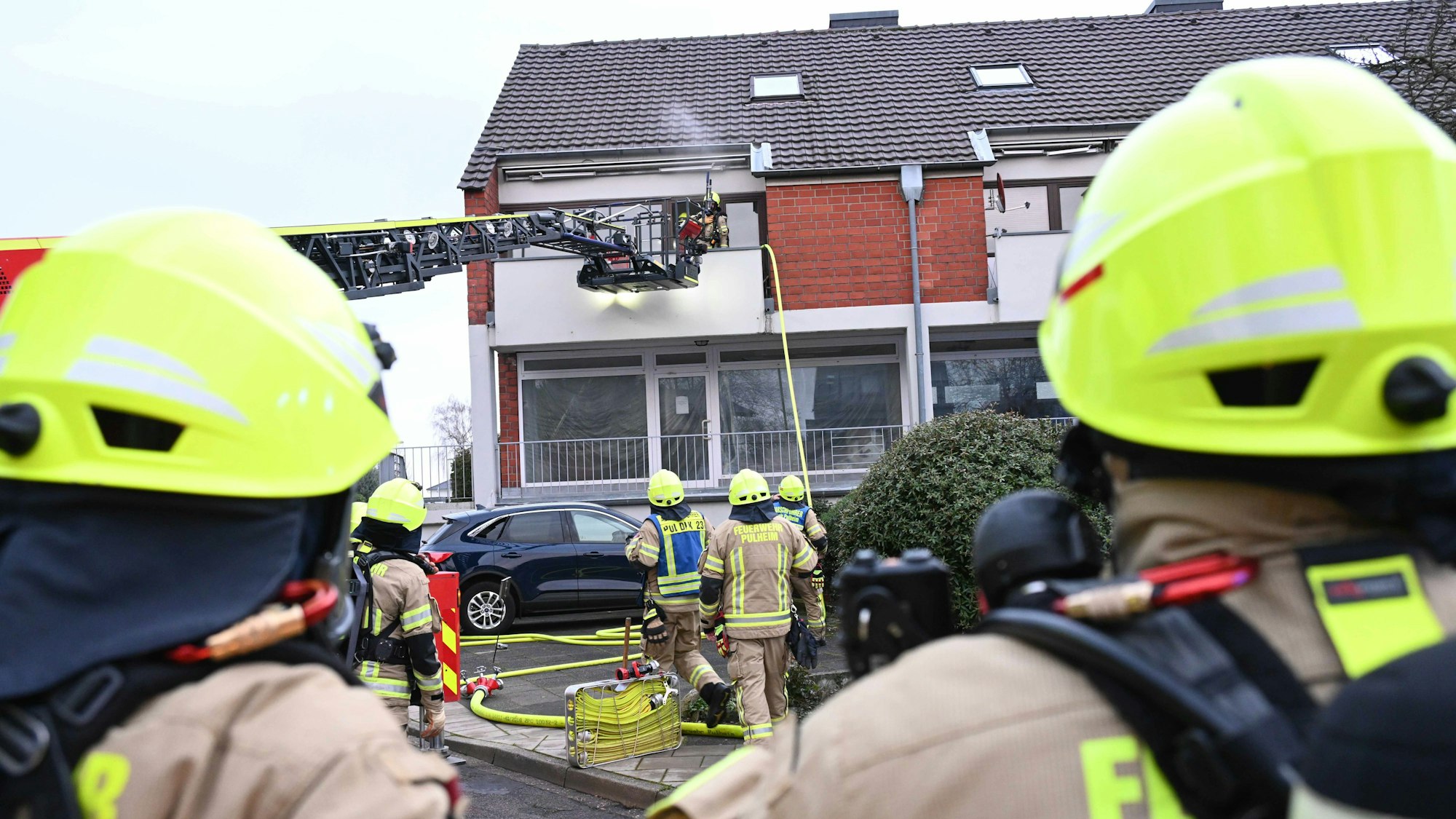 Einsatzkräfte der Feuerwehr mit einer Drehleiter vor einem Mehrfamilienhaus.
