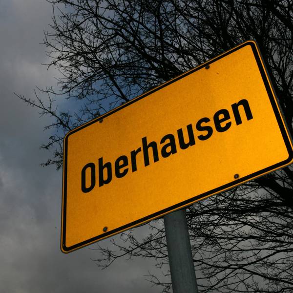 Das Ortsschild von Oberhausen steht vor düsterem Himmel und den dürren, blattlosen Ästen eines Baumes. (Symbolbild)
