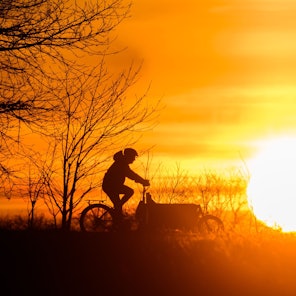 Ein Mann fährt bei Sonnenaufgang mit einem Lastenfahrrad über einen Feldweg in der Region Hannover.