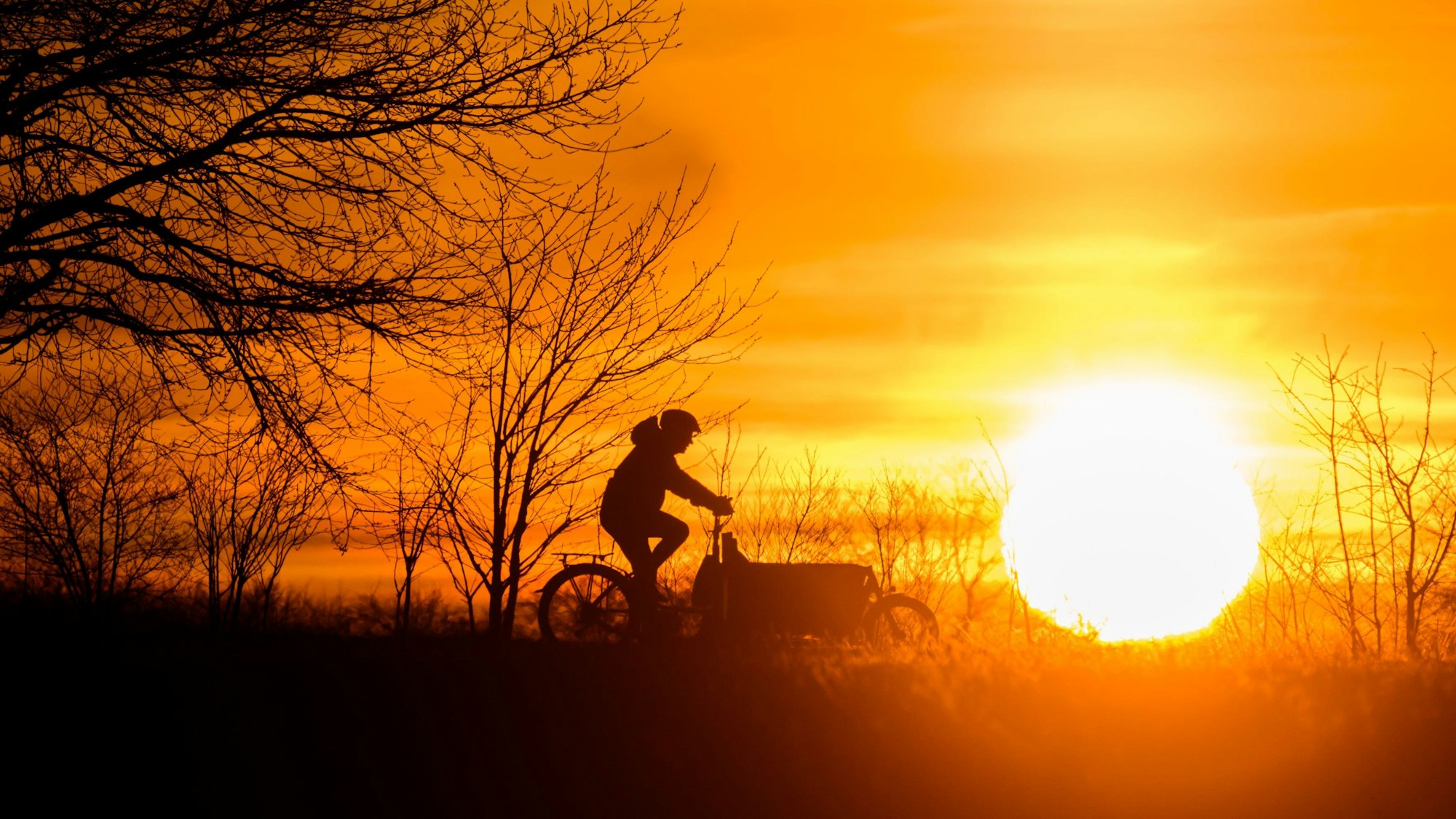 Ein Mann fährt bei Sonnenaufgang mit einem Lastenfahrrad über einen Feldweg in der Region Hannover.