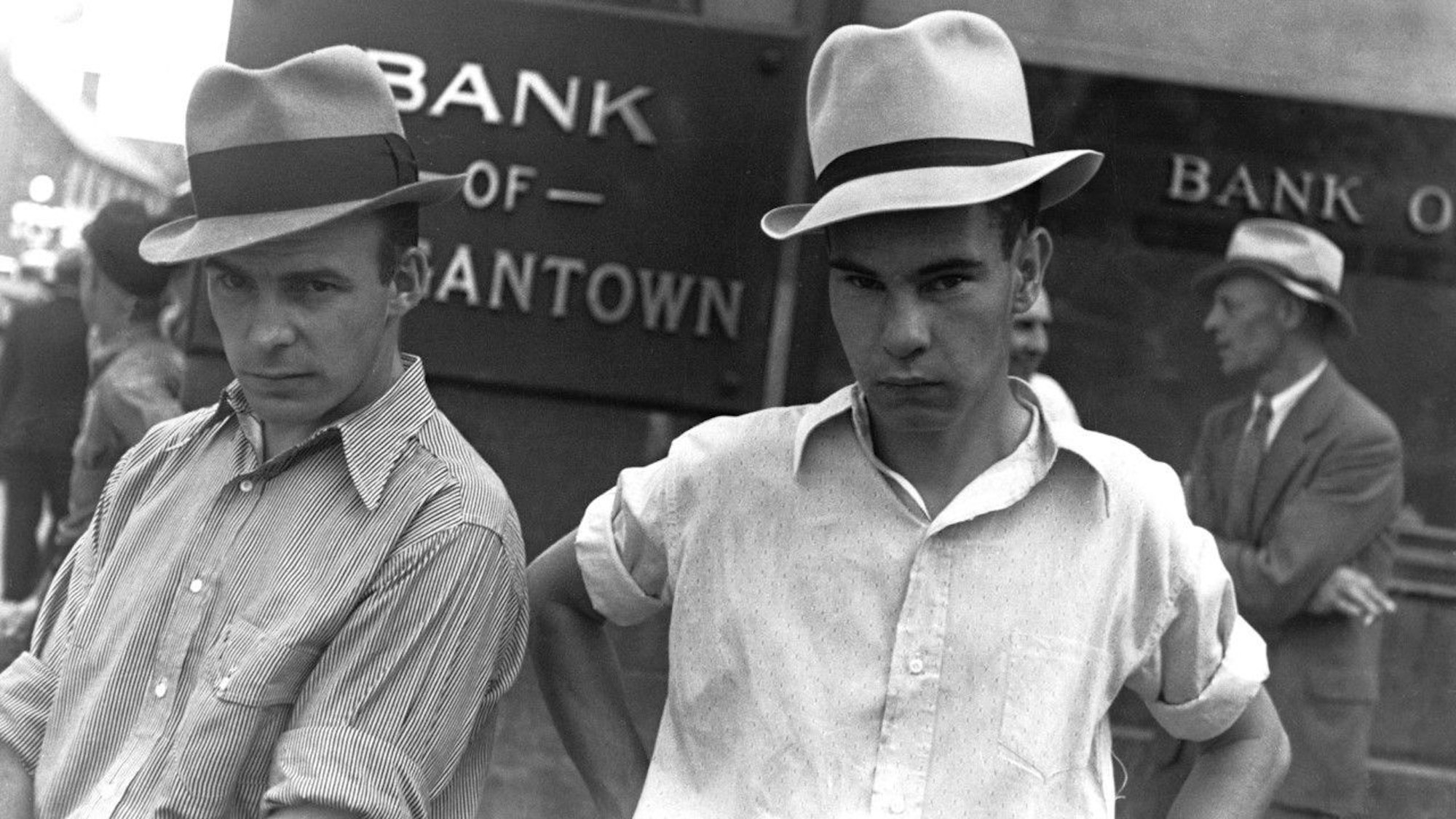 Die Schwarz-Weiß-Aufnahme „Main Street, Morgantown, West Virginia, 1935“ von Walker Evans zeigt zwei Männer, die Hüte tragen und vor einem Bankgebäude stehen.