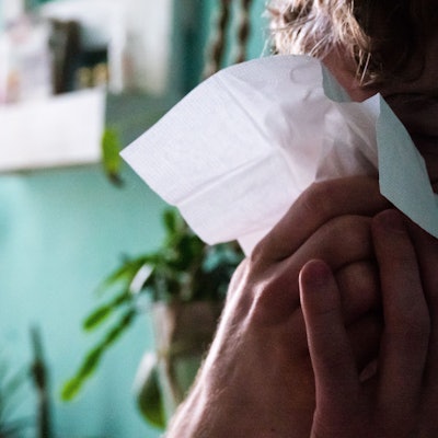 Eine Frau niest in ein Taschentuch.