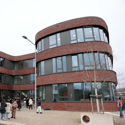 Ein Schulgebäude mit geschwungenen Formen und davor Schülerinnen und Schüler.