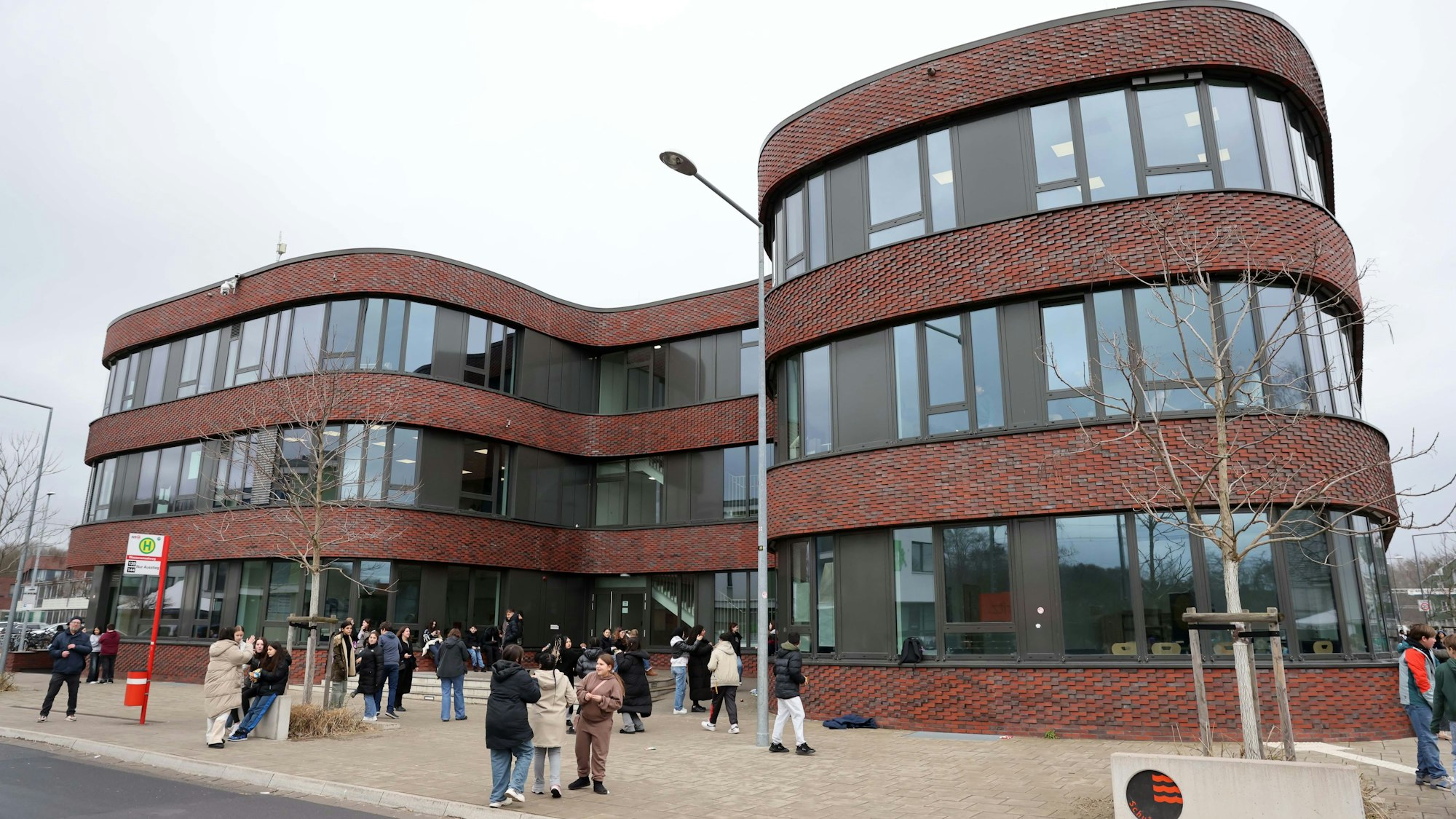 Schülerinnen und Schüler stehen vor einem gewundenen Schulgebäude.
