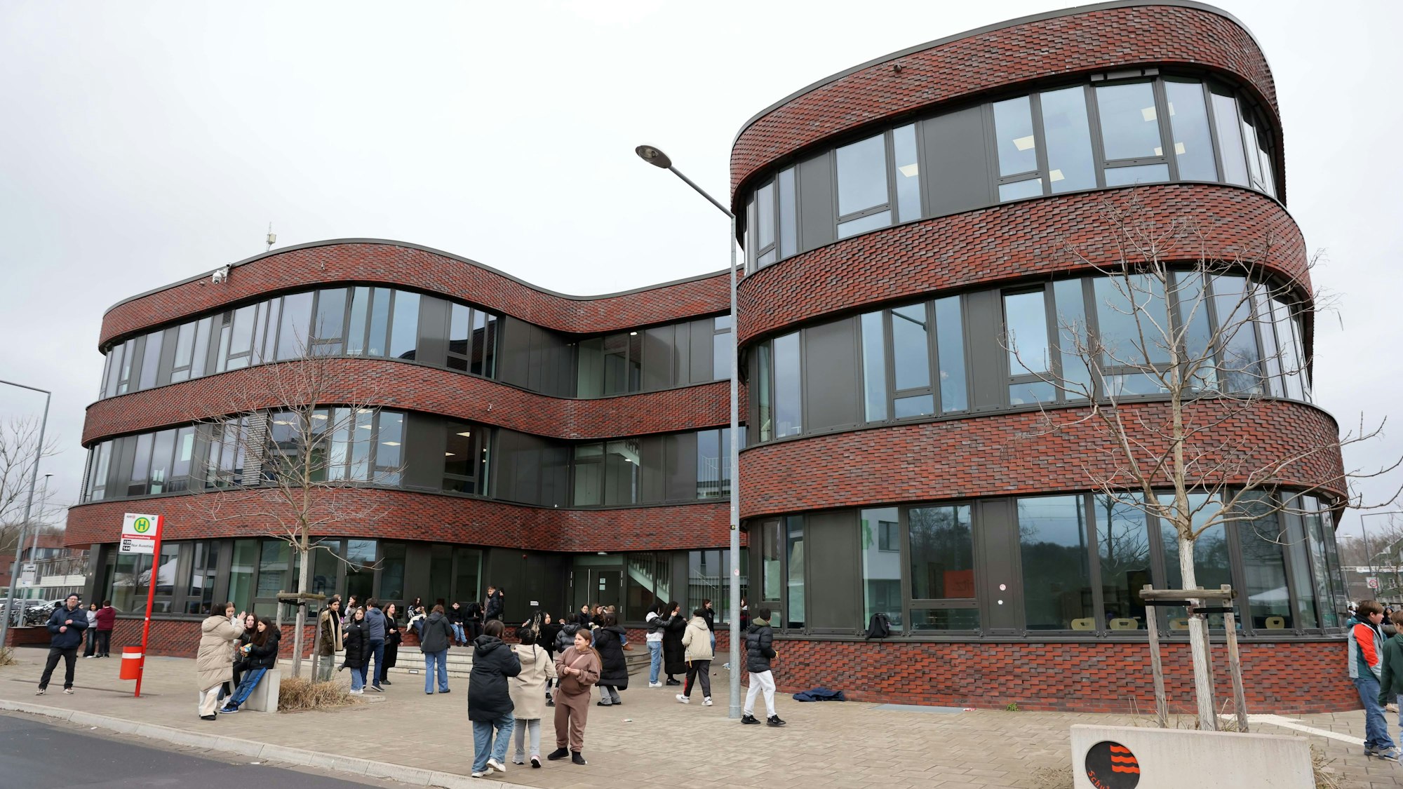 Schüler warten vor dem geschwungenen Schulgebäude.