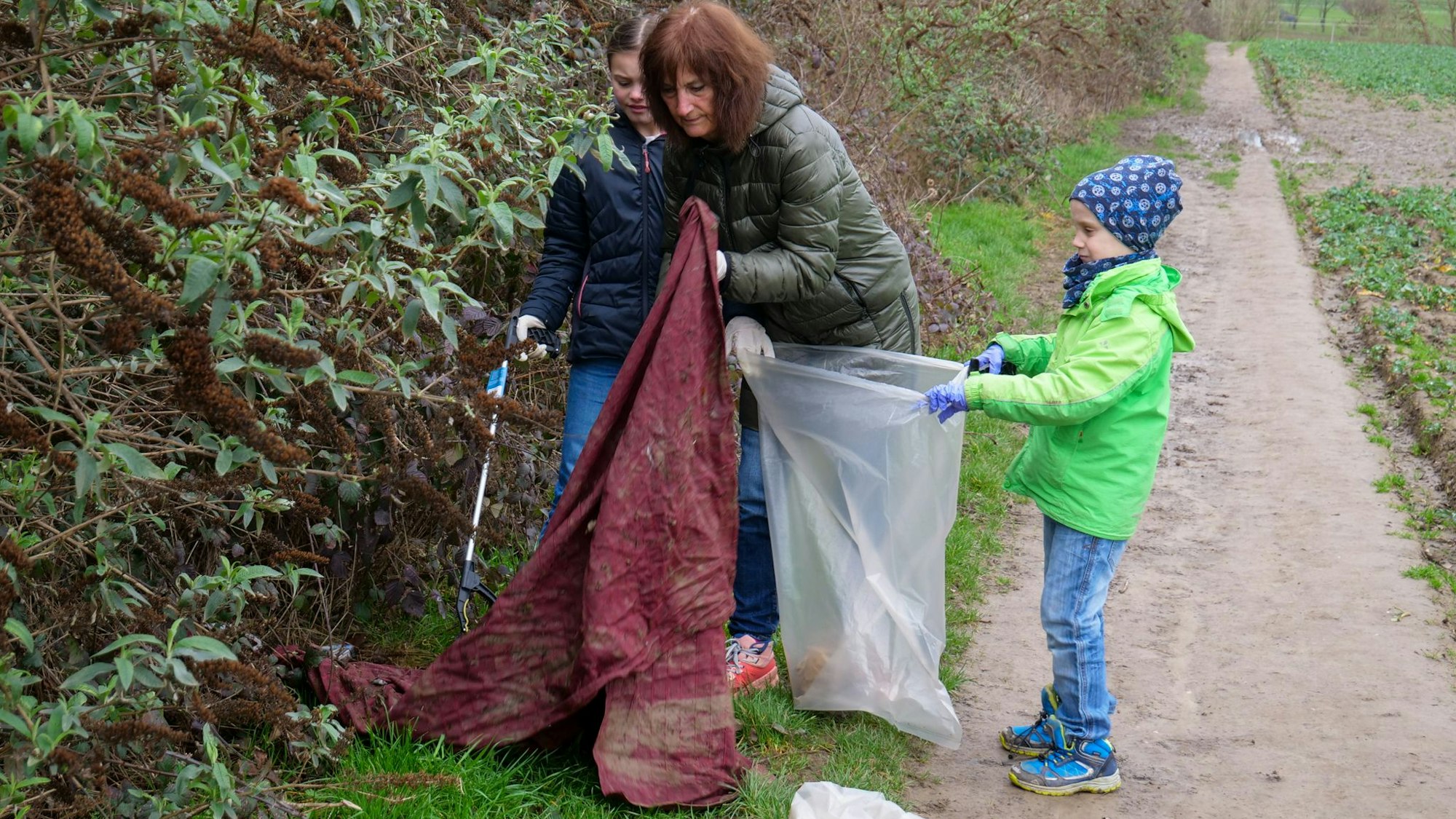 Auf dem Foto ist eine Frau mit zwei Kindern zu sehen, die Müll in einen Sack stopfen.