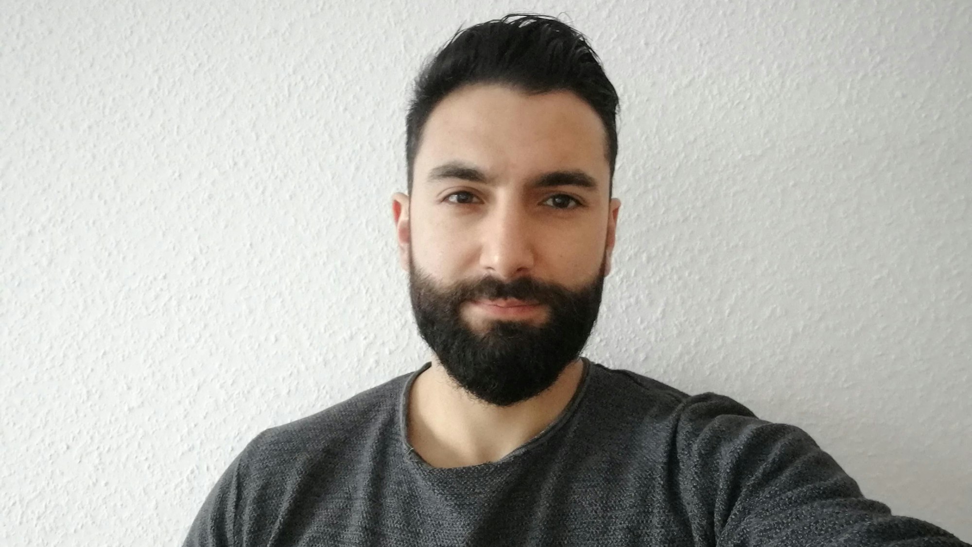 Ein dunkelhaariger Mann mit Bart lächelt leicht.