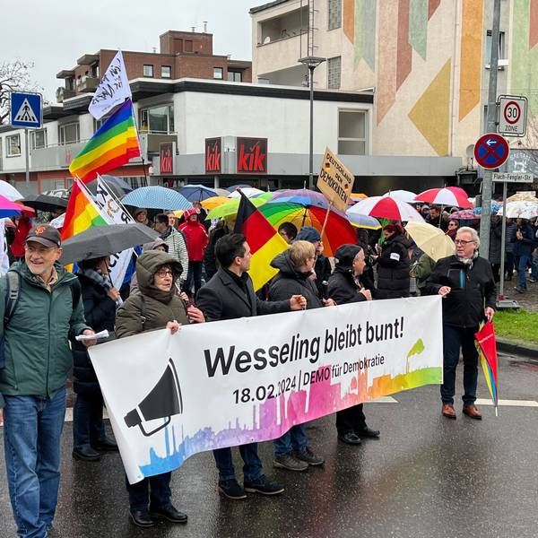 Auf dem Foto sind Teilnehmer der Demonstration gegen Rechtsextremismus in Wesseling zu sehen. Auf einem Banner steht „Wesseling bleibt bunt!“