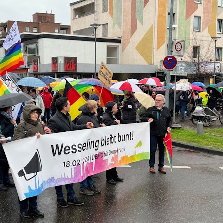 Auf dem Foto sind Teilnehmer der Demonstration gegen Rechtsextremismus in Wesseling zu sehen. Auf einem Banner steht „Wesseling bleibt bunt!“