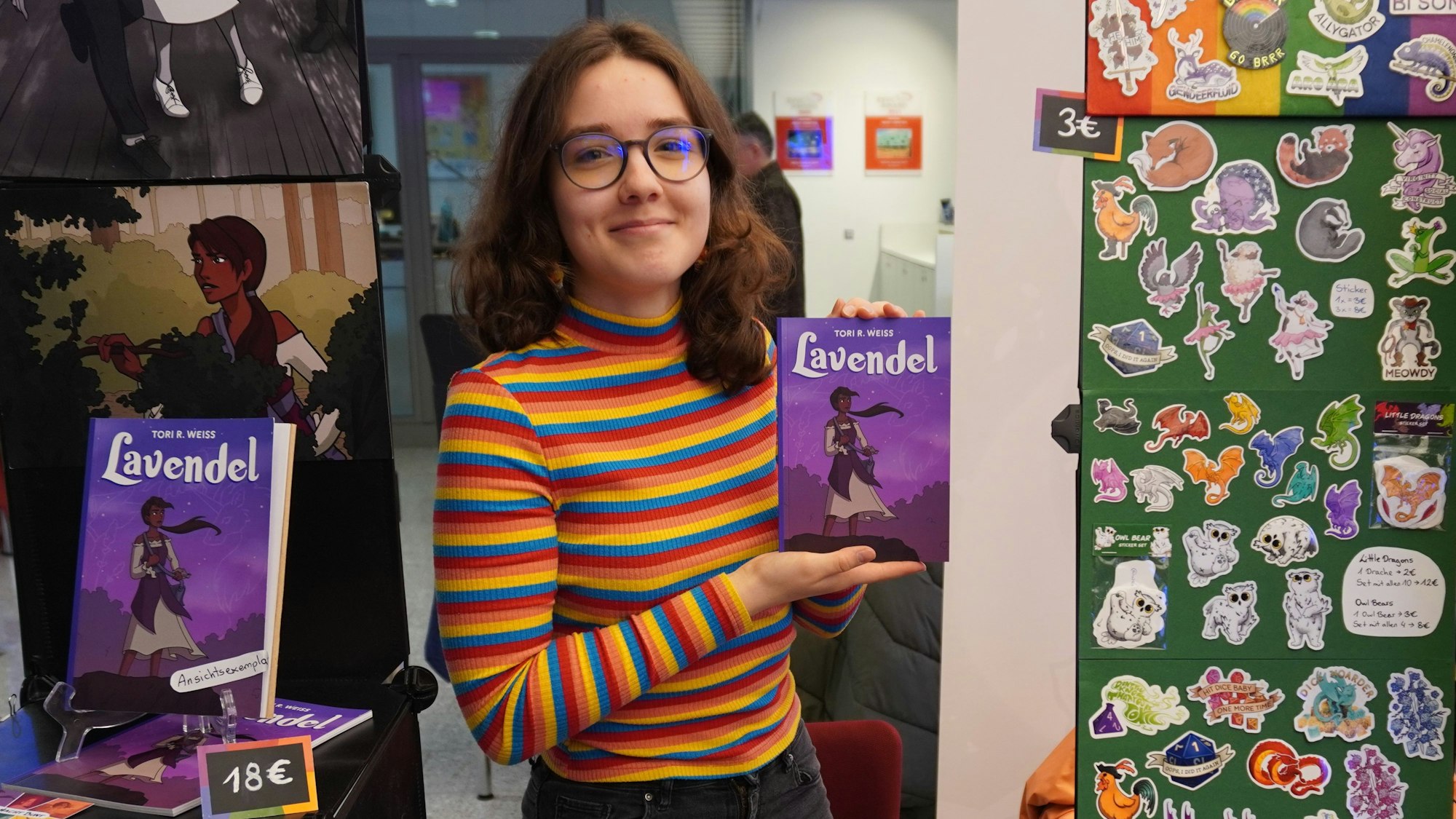 Auf dem Foto ist Tori Weiss zu sehen. Sie zeigt einen Comic, den sie im Selbstverlag herausgebracht hat.