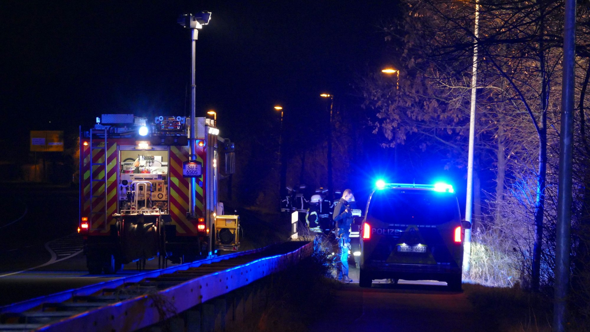 Ein Feuerwehrauto steht auf einer Straße, ein Polizeiwagen auf einem Radweg.