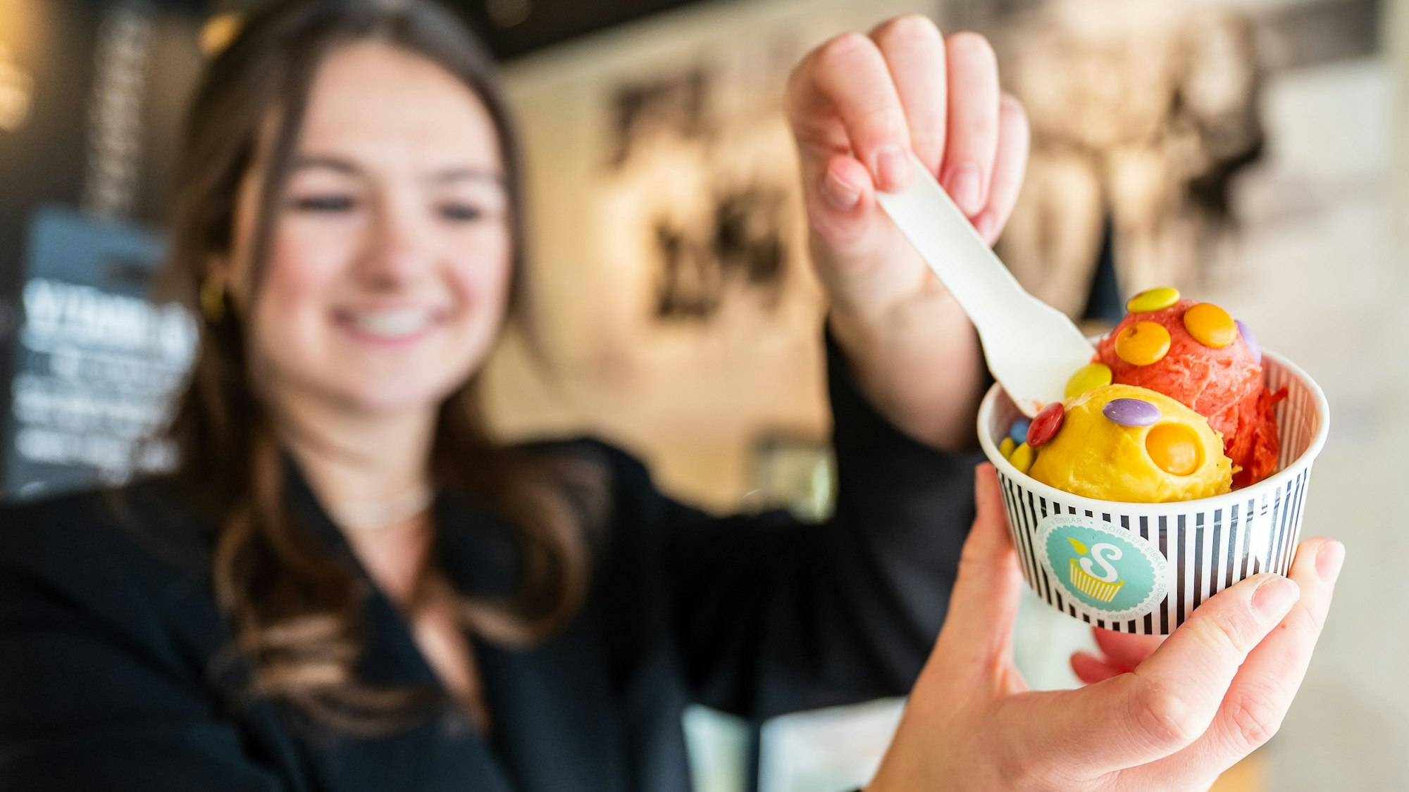 Die Besitzerin eines Eiscafés hält einen Becher mit zwei Kugeln Fruchteis. (Symbolbild)