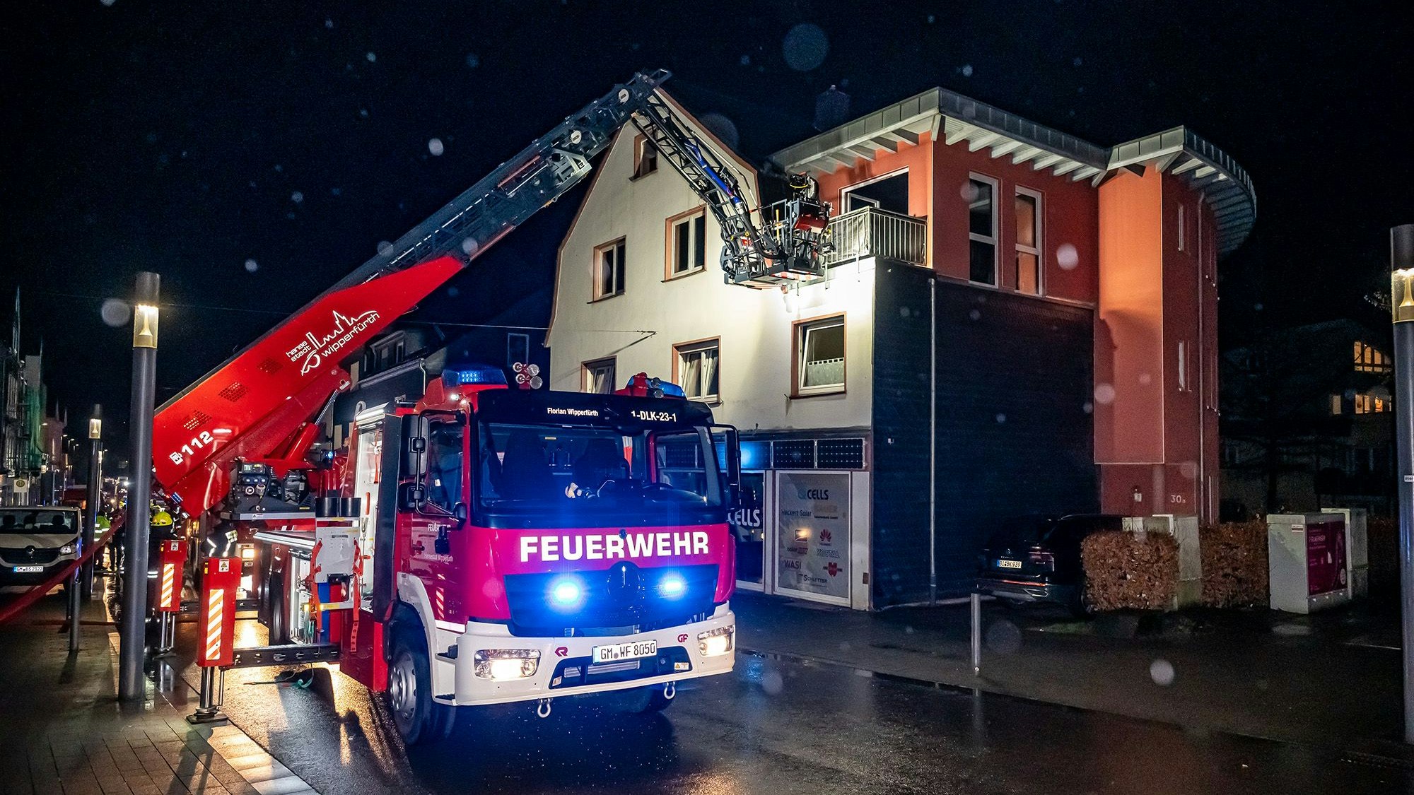 Ein Feuerwehrauto mit Drehleiter. Über diese löschen Einsatzkräfte einen Brand über einen Balkon eines Wohnhauses.
