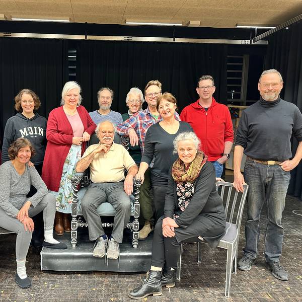 Eine Theatergruppe steht und sitzt auf einer Bühne.
