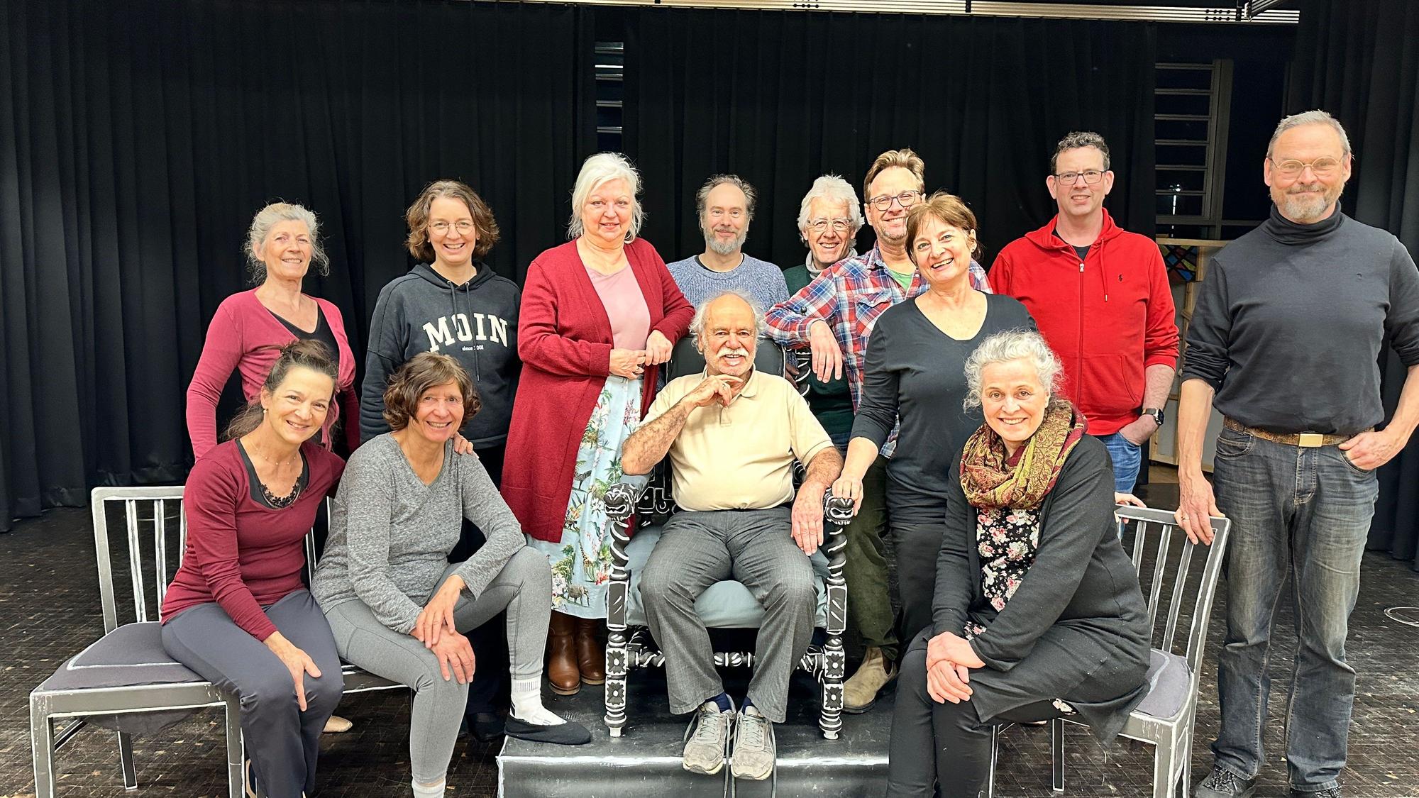 Eine Theatergruppe steht und sitzt auf einer Bühne.