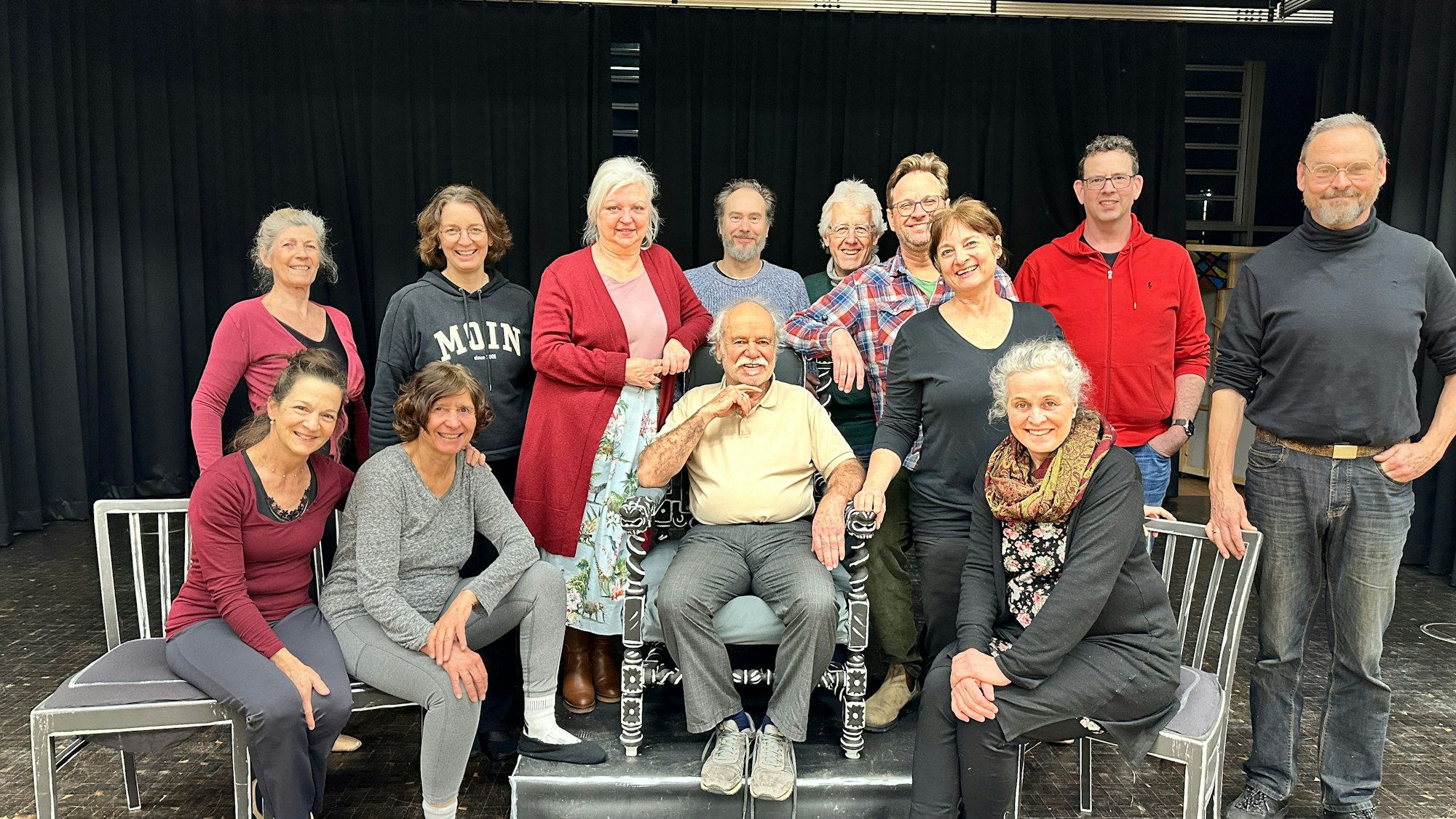 Eine Theatergruppe steht und sitzt auf einer Bühne.