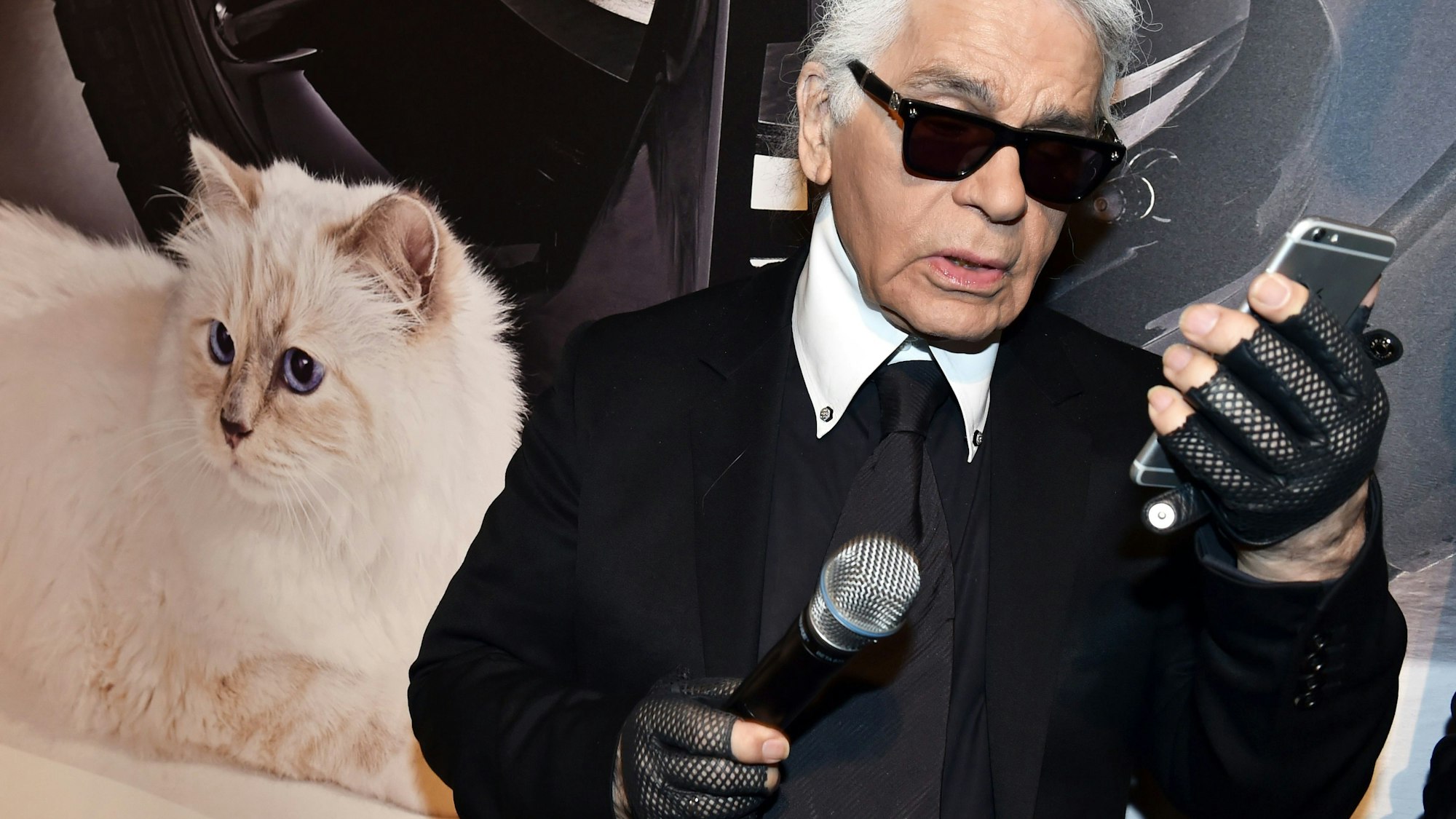 Der Modedesigner Karl Lagerfeld blickt neben einem Foto seiner Birma-Katze Choupette auf sein Smartphone (Archivbild)