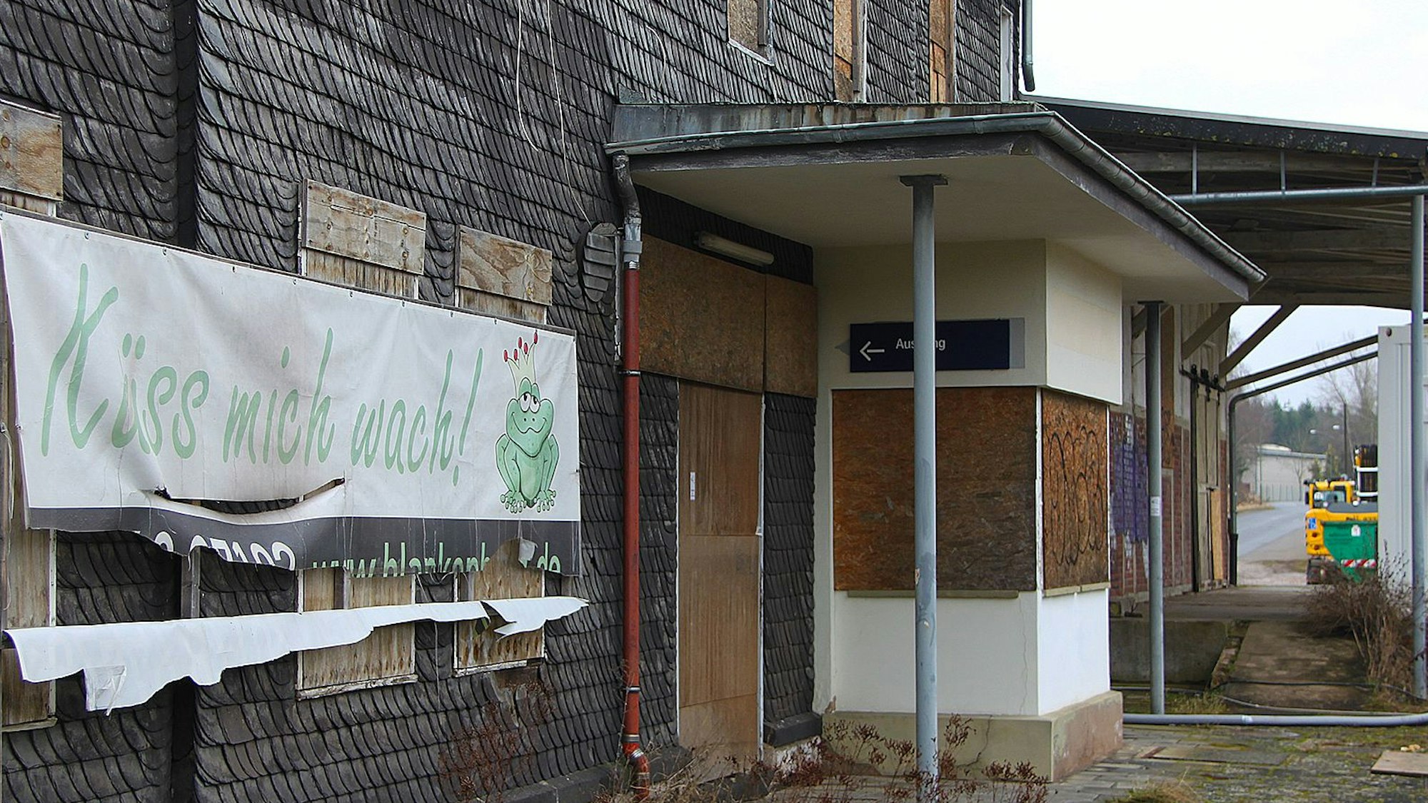 Ein Plakat mit der Aufschrift „Küss mich wach“ hängt an der Fassade des Bahnhofs Blankenheim-Wald. Der untere Teil ist bereits zerrissen.