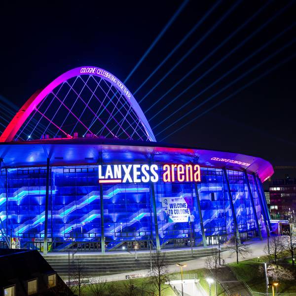 Illumination der Lanxess-Arena zur Handball-Europameisterschaft im Januar. Die Halle erstrahlt in blauem Licht, der Bogen ist rosa angestrahlt.