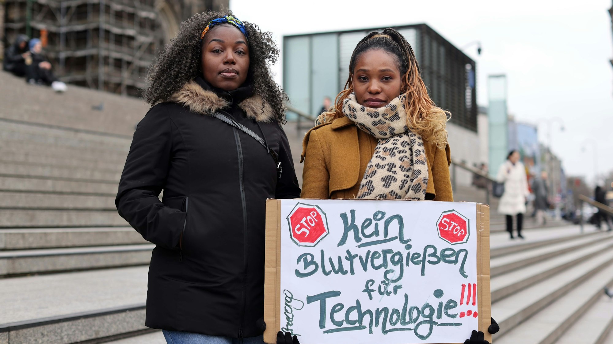 Zwei Frauen halten ein Schild mit der Aufschrift „Kein Blutvergießen für Technologie“.