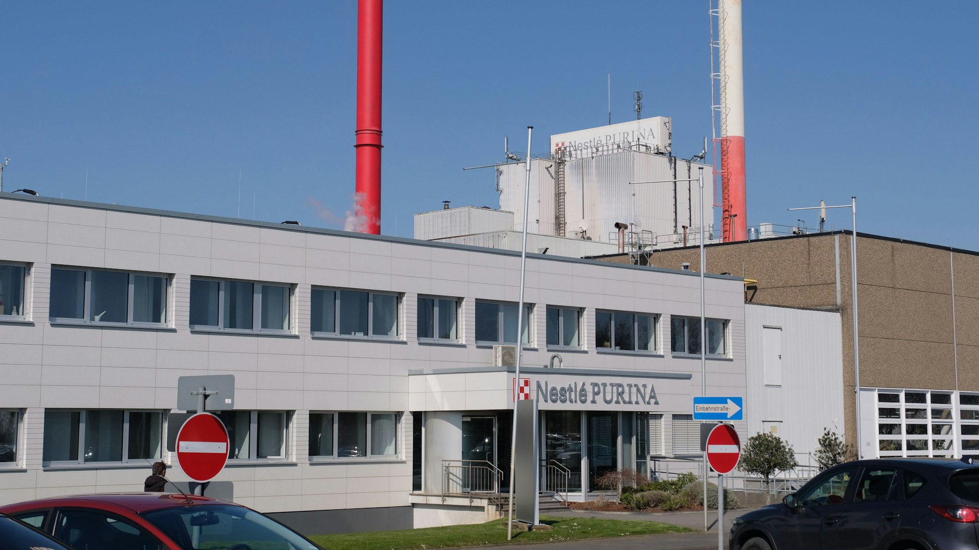 Das Bild zeigt den Eingang zum Verwaltungstrakt der Fabrik, im Hintergrund zwei Schornsteine.