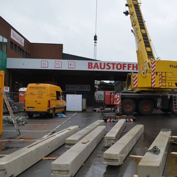 Ein Spezialkran wuchtet in Waldbröl bis Donnerstag fertige Betonteile für eine neue Halle im Baucentrum Cronrath auf ihren Platz. Hier liegen schon die Betonpfeiler parat, die gleich aufgestellt werden. Unser Foto zeigt die Baustelle von außen und den Kran davor.