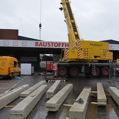 Ein Spezialkran wuchtet in Waldbröl bis Donnerstag fertige Betonteile für eine neue Halle im Baucentrum Cronrath auf ihren Platz. Hier liegen schon die Betonpfeiler parat, die gleich aufgestellt werden. Unser Foto zeigt die Baustelle von außen und den Kran davor.