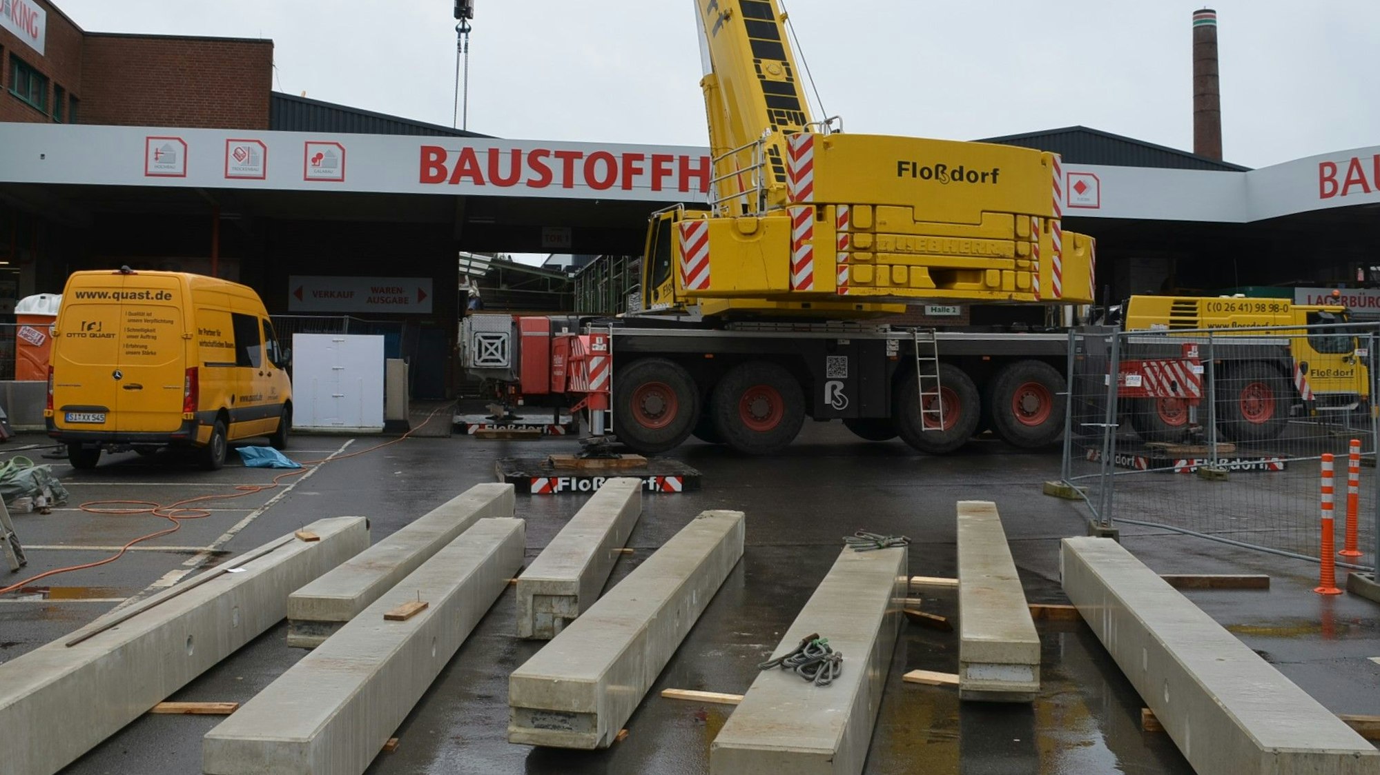 Ein Spezialkran wuchtet in Waldbröl bis Donnerstag fertige Betonteile für eine neue Halle im Baucentrum Cronrath auf ihren Platz. Hier liegen schon die Betonpfeiler parat, die gleich aufgestellt werden. Unser Foto zeigt die Baustelle von außen und den Kran davor.