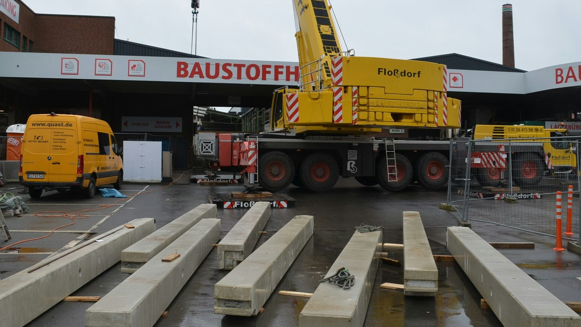 Ein Spezialkran wuchtet in Waldbröl bis Donnerstag fertige Betonteile für eine neue Halle im Baucentrum Cronrath auf ihren Platz. Hier liegen schon die Betonpfeiler parat, die gleich aufgestellt werden. Unser Foto zeigt die Baustelle von außen und den Kran davor.