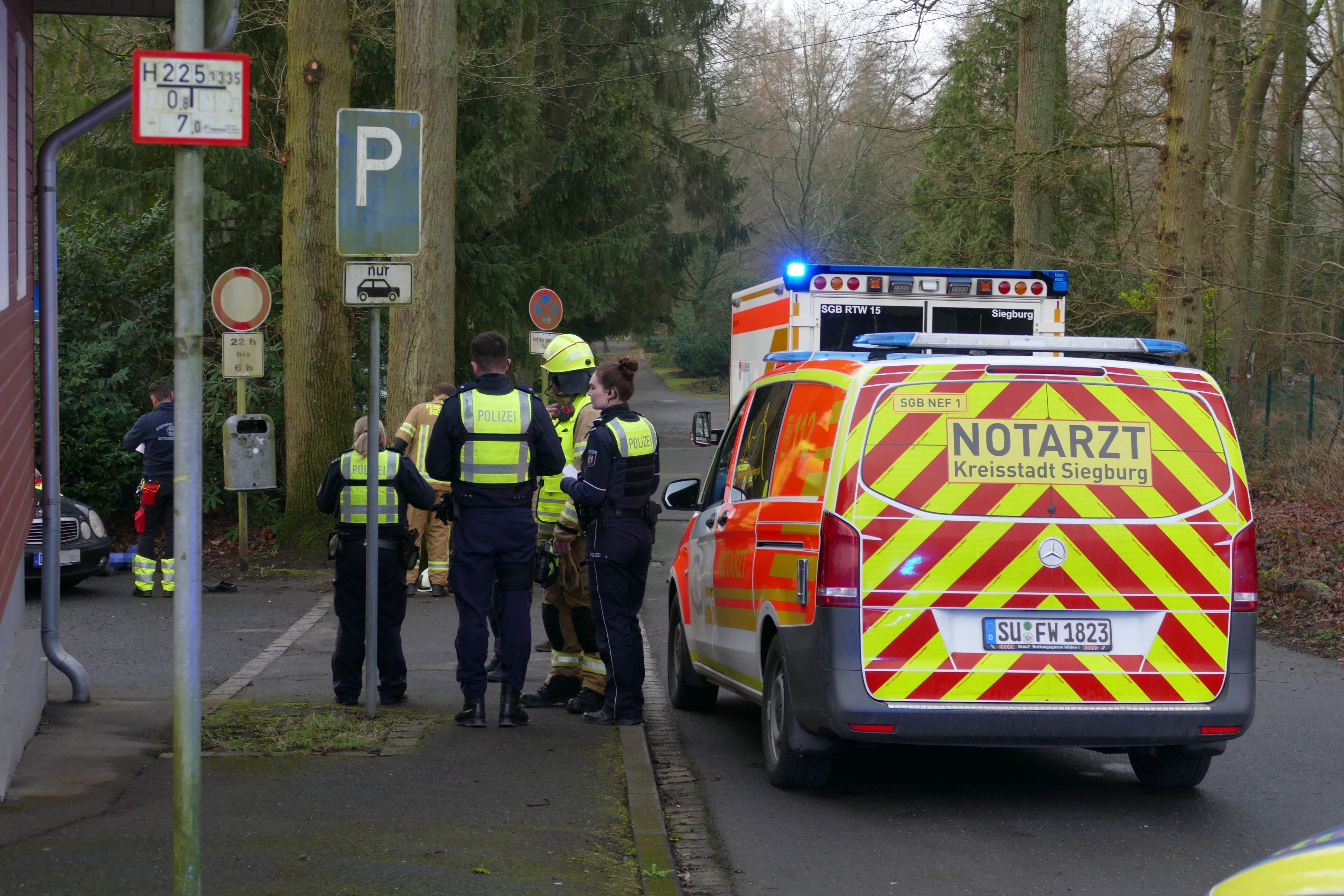 Polizsiten und Feuerwehrleute stehen neben einem Notarztfahrzeug.