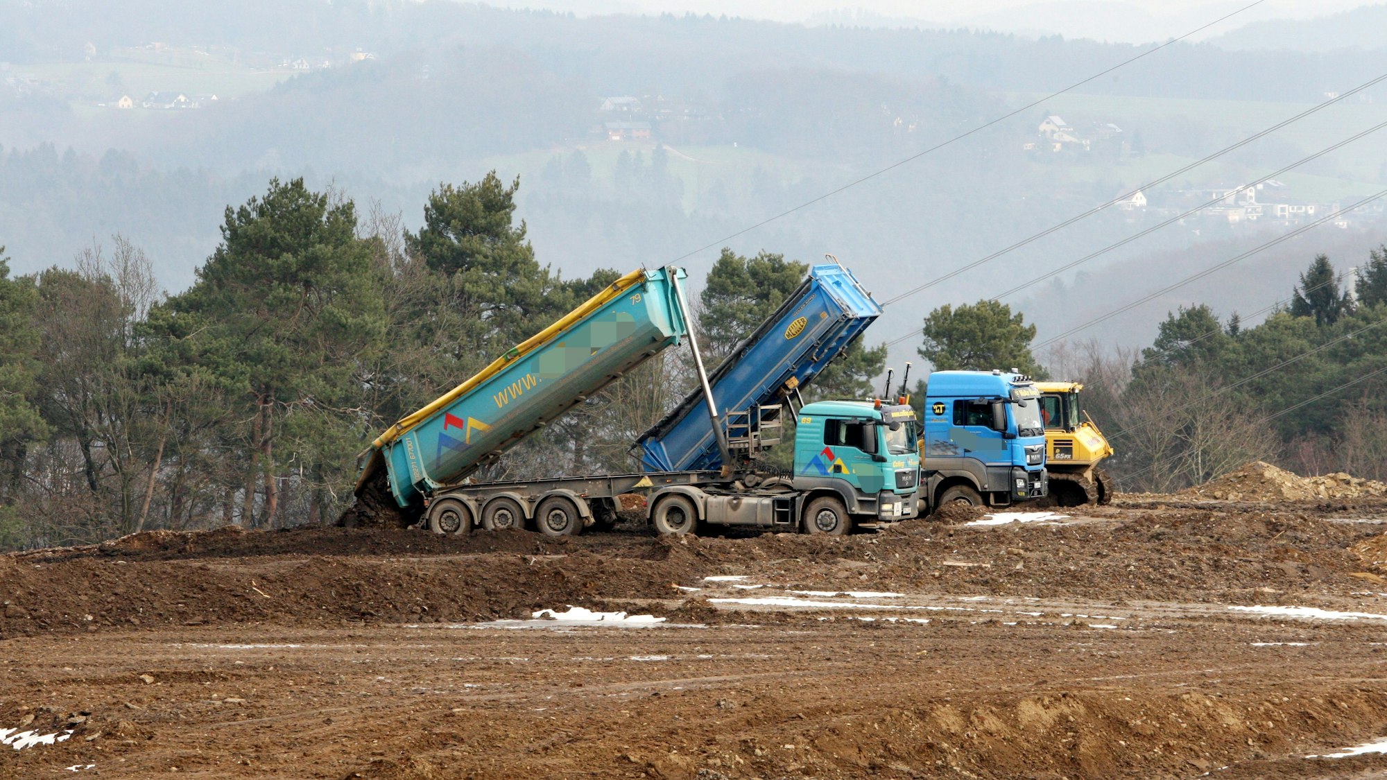 Zwei Lastwagen kippen Erde auf einer Erddeponie ab.