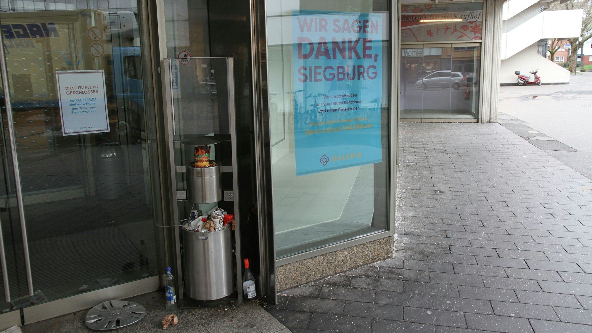 Ein überquellender Mülleimer neben dem Eingang eines geschlossenen Kaufhauses