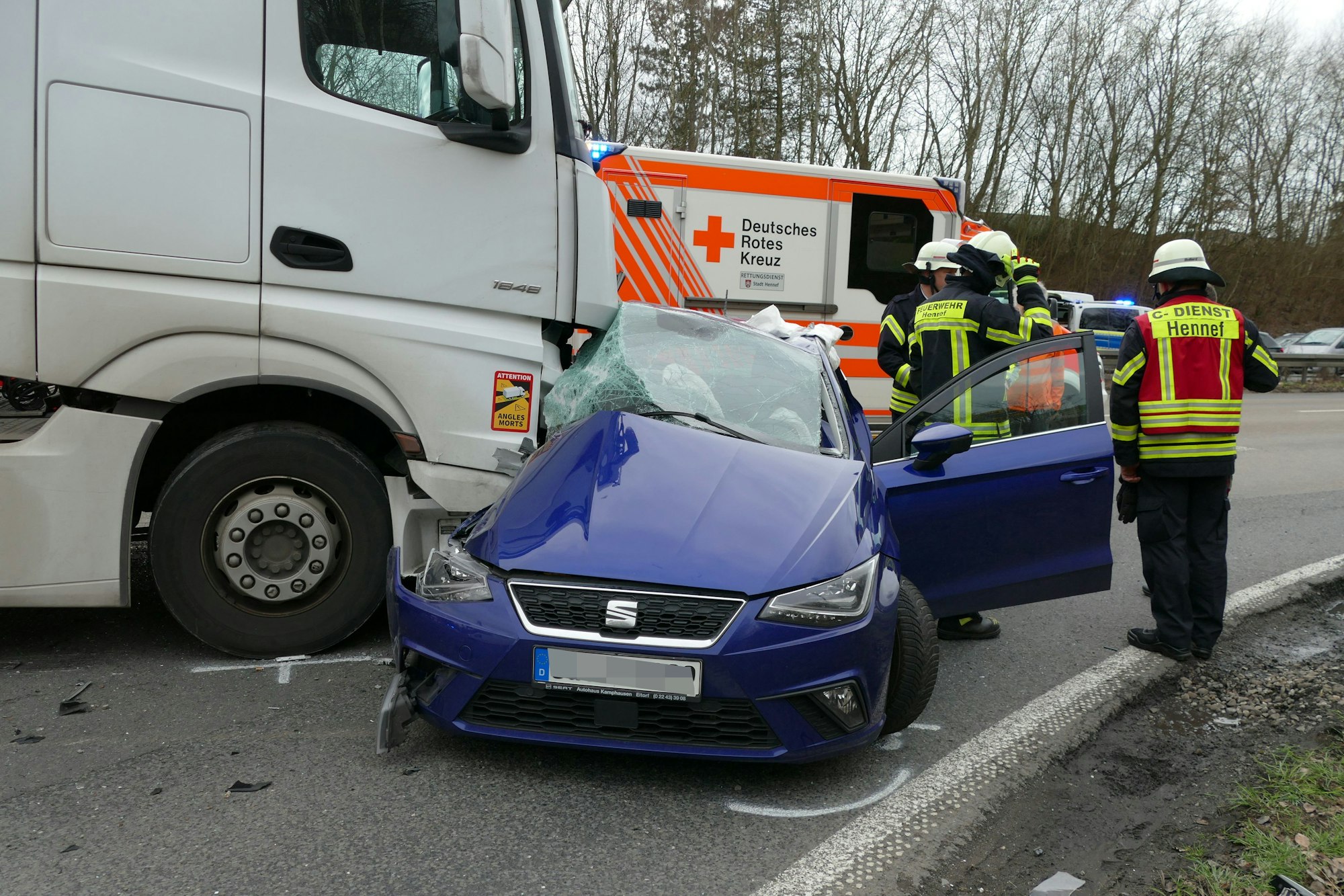 Ein Lkw hat ein Auto gerammt, daneben stehen Feuerwehrleute.