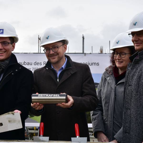 Bürgermeister und Beigeordneter halten Stein und Mörtel, sowie Zeitkapsel in der Hand.