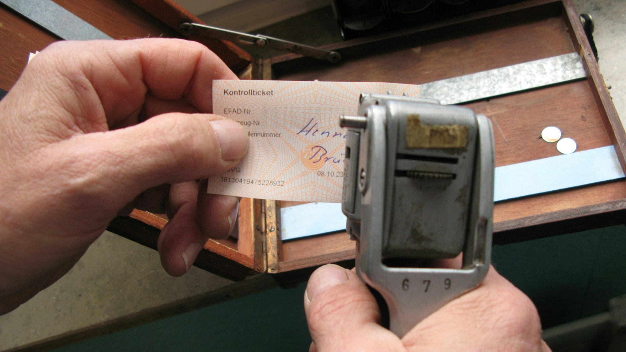 Zwei Hände, die eine hält eine Fahrkarte, die andere eine alte Zange zum Abknipsen der Fahrkarte.
