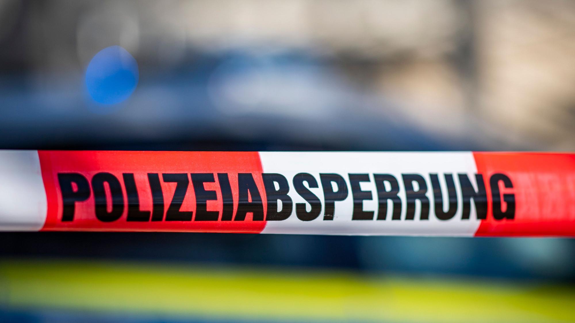 ARCHIV - 28.09.2021, Nordrhein-Westfalen, Gütersloh: Ein Absperrband mit der Aufschrift „Polizeiabsperrung“ ist vor einem Polizeiwagen aufgespannt.
