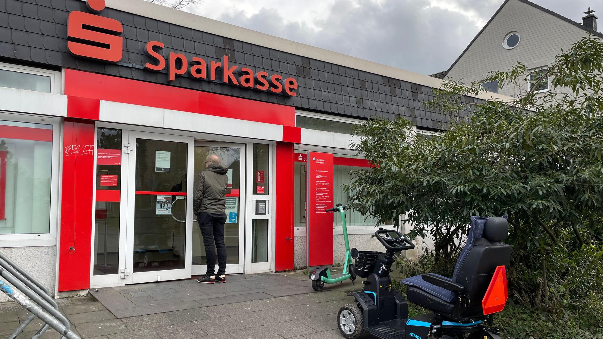 Ein Mann steht vor der Glastür einer kleinen Sparkassen-Filiale.