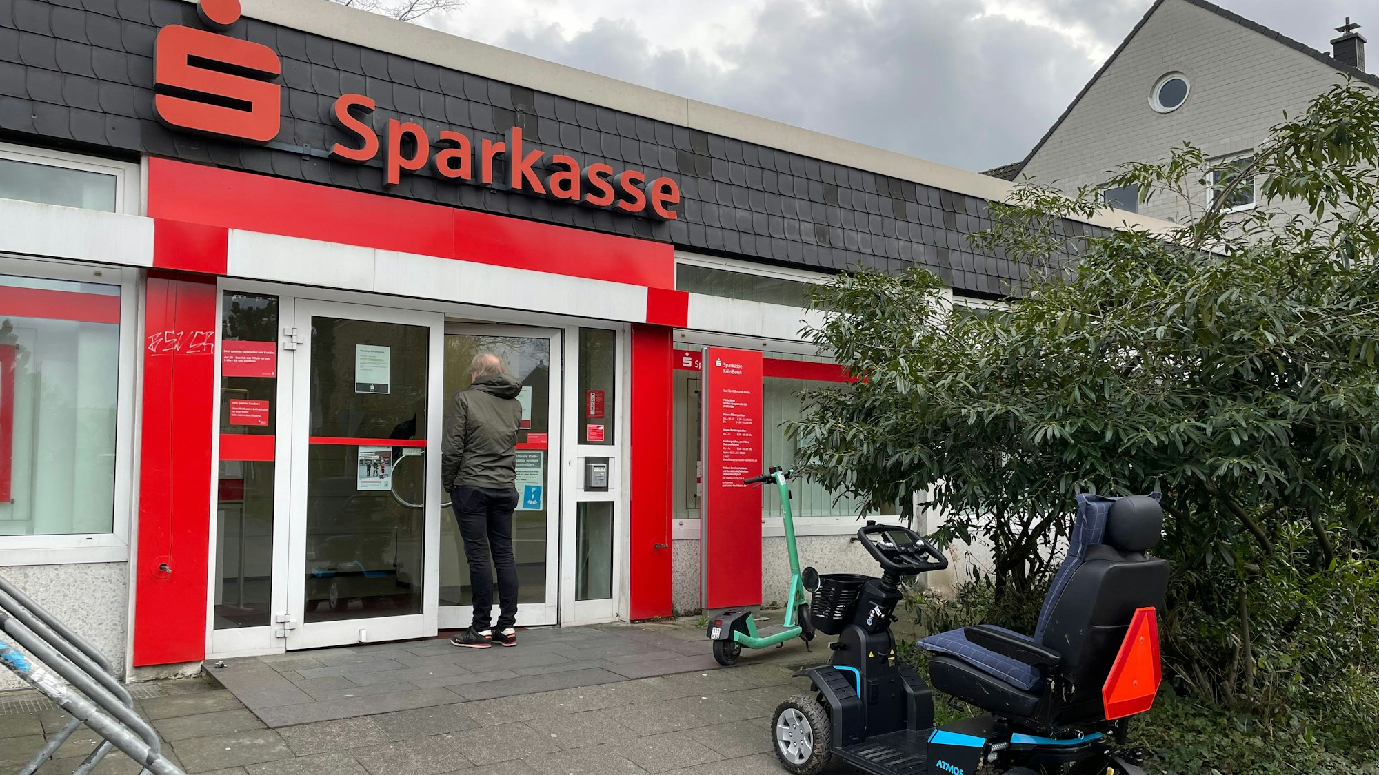 Ein Mann steht vor der Glastür einer kleinen Sparkassen-Filiale.