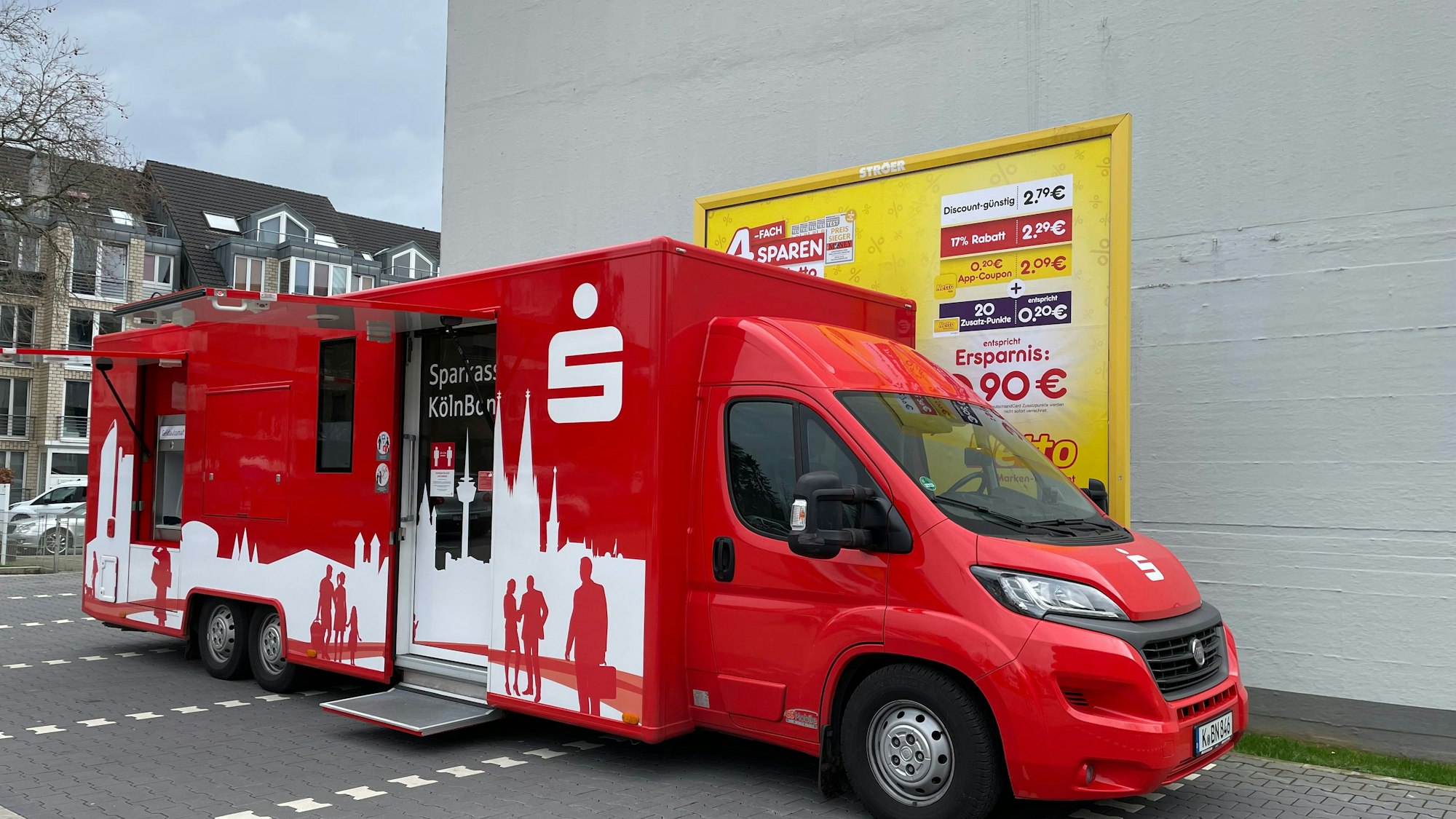 Ein Sparkassen-Bus steht auf einem Supermarkt-Parkplatz.