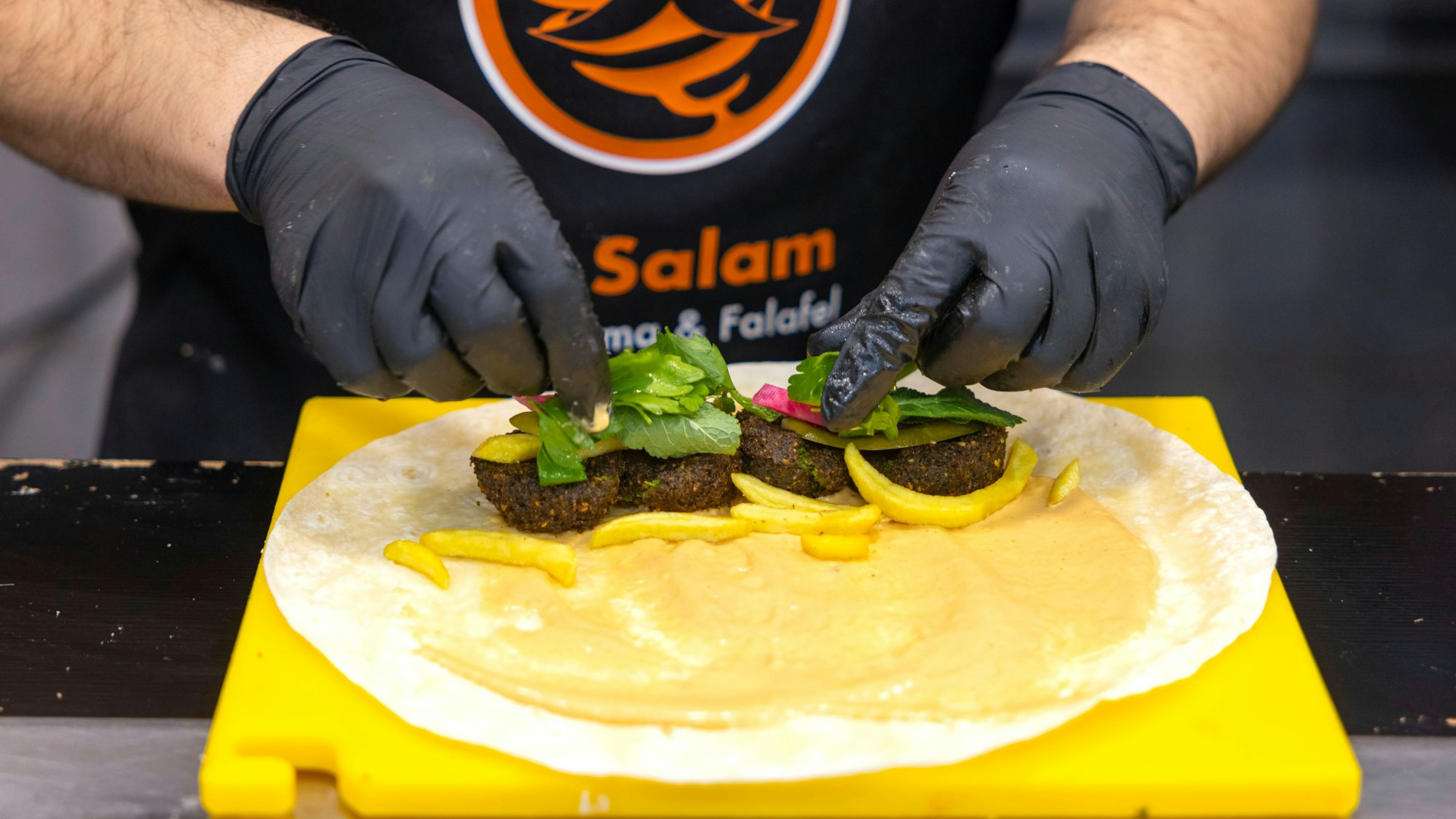Zu den Falafel-Bällchen kommen Pommes, Minze und eingelegtes Gemüse in das dünne Fladenbrot.