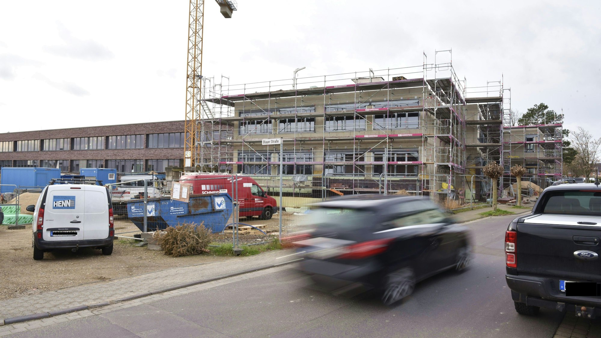 Ein Auto fährt an dem eingerüsteten Bau am Zülpicher Schulcampus vorbei.