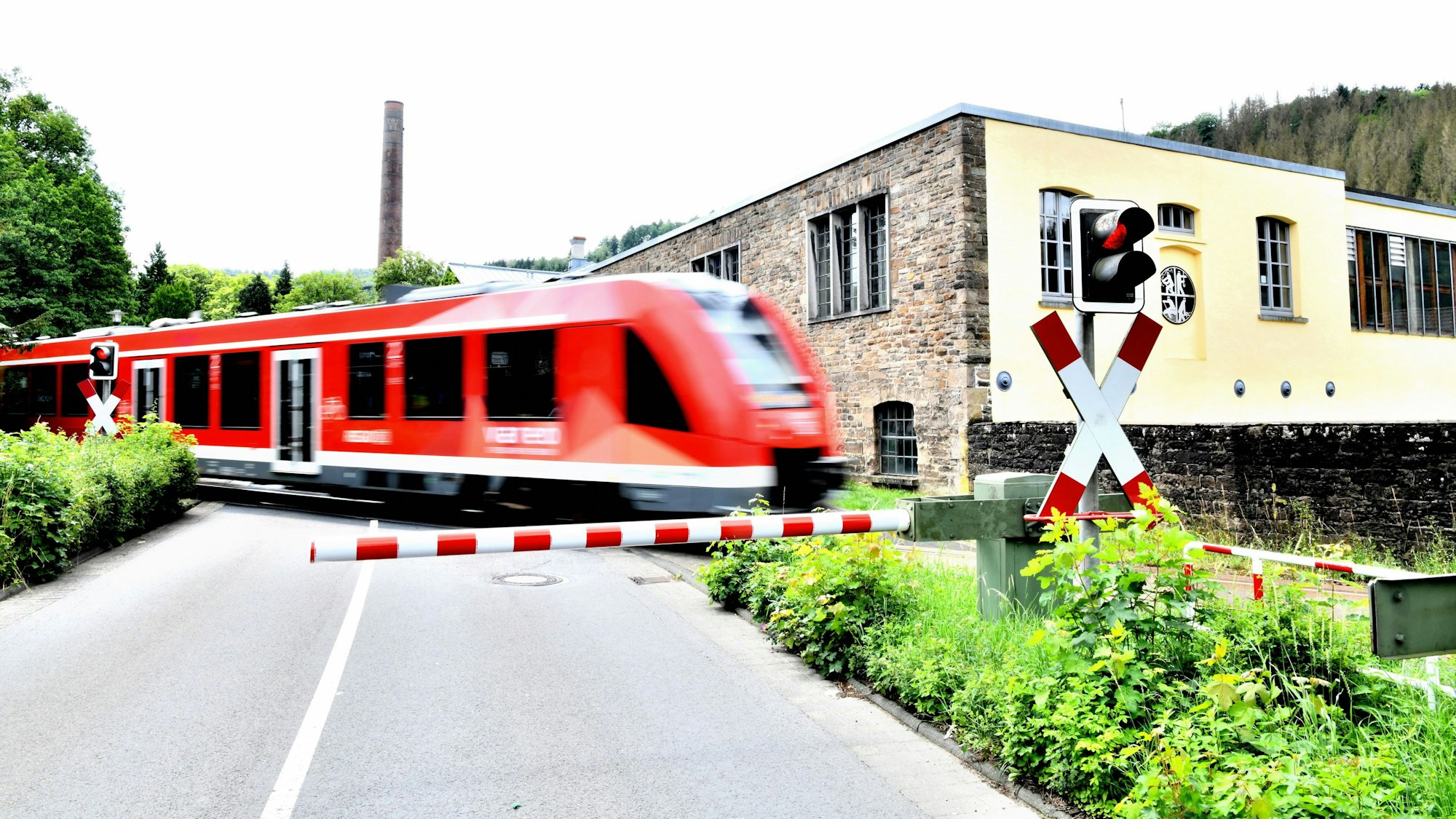 Ein Zug der Regionalbahn 25 passiert den Bahnübergang Märkische Straße in Engelskirchen, im Hintergrund die Fabrik Ermen und Engels, wo heute das Industriemuseum und das Rathaus zu finden sind.