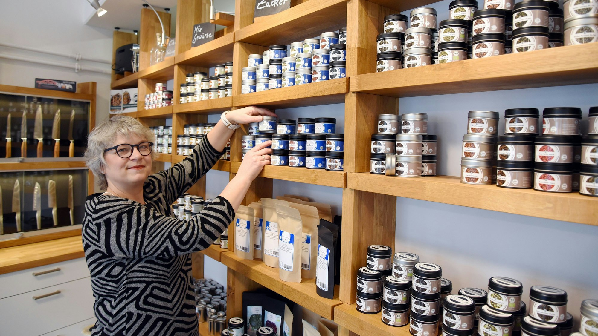Eine Frau sortiert Gewürzdosen in einem Regal.